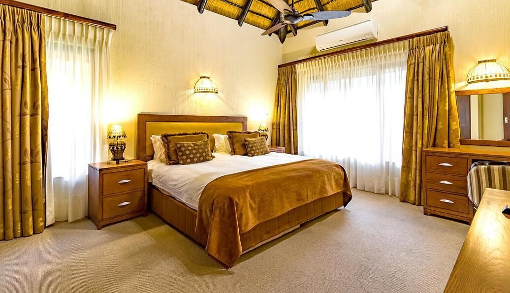 Quarto de hotel com uma cama grande, duas mesas de cabeceira com luminárias, um painel de cama de madeira e um espelho grande.