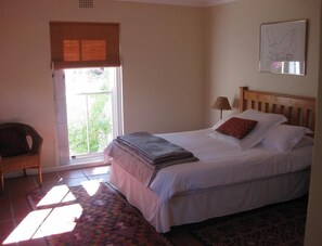 A bedroom with a bed, a chair, a window with blinds, and a wall-mounted lamp. - Sunny Lane (Franschhoek)