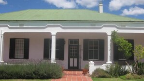 A white building with a green roof, a central entrance with a door, and a small porch area. - Sunny Lane (Franschhoek)