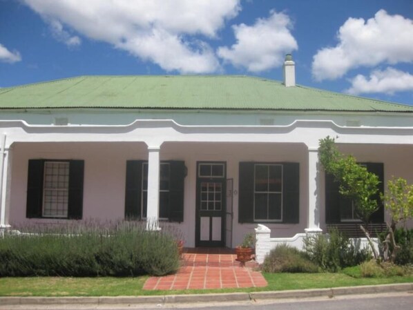 A white building with a green roof, a central entrance with a door, and a small porch area. - Sunny Lane (Franschhoek)