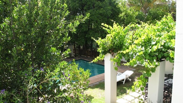 A backyard with a swimming pool, surrounded by lush greenery and white pillars. - Sunny Lane (Franschhoek)
