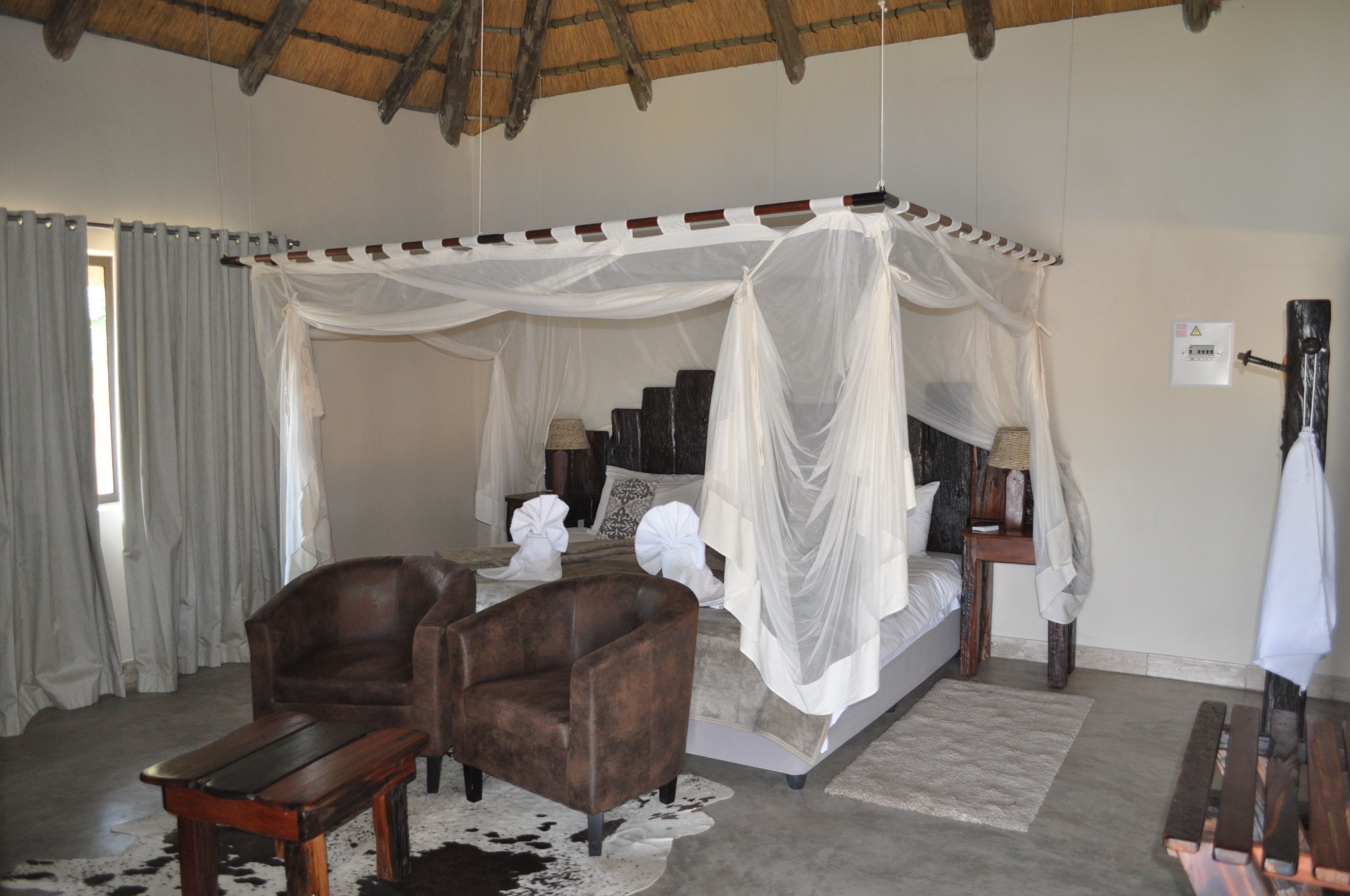 A bedroom with a four-poster bed, a wooden bench, a chair, and a cowhide rug.