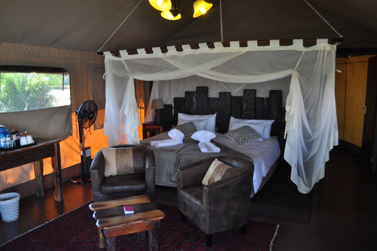A tent-style room with a bed, two sofas, a table with bottles, and a lamp.