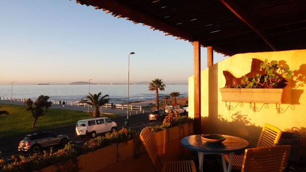 A balcony with a view of the ocean, outdoor seating, and a planter with greenery. - Dolphin Inn Guest House (Cape Town)
