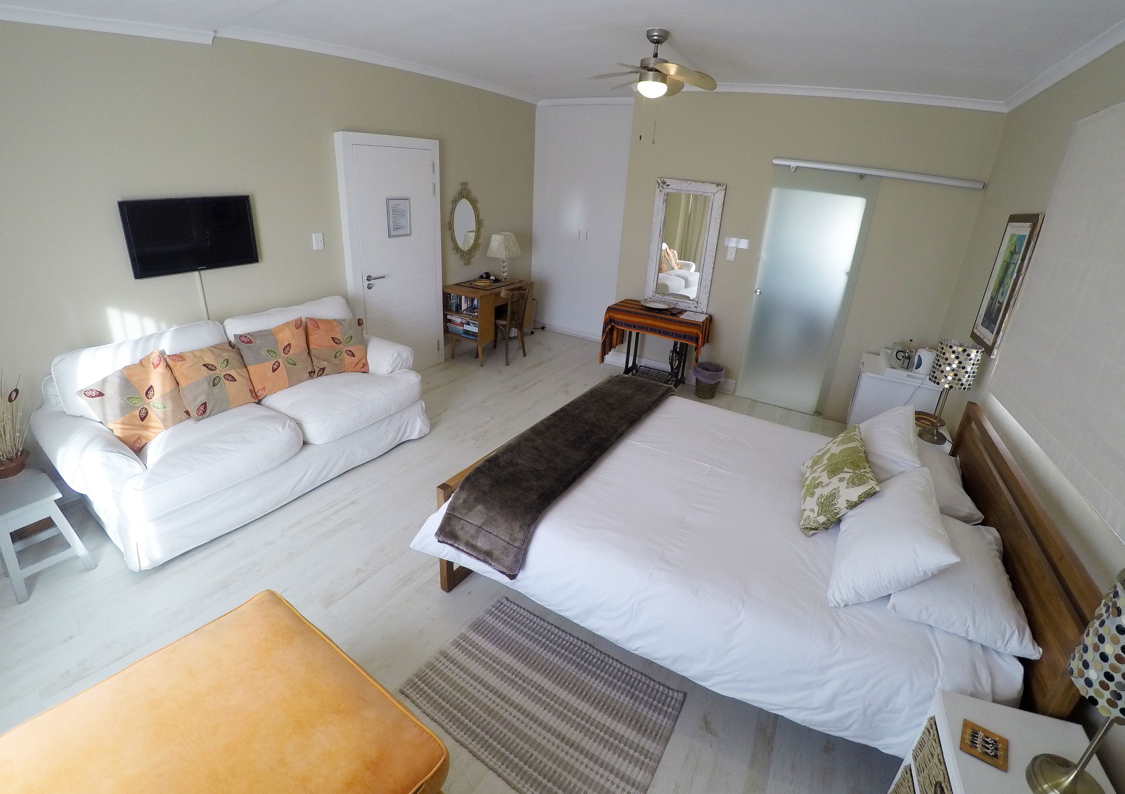 Ein Hotelzimmer mit einem großen Bett, einer Couch, einem Schreibtisch, einem Fernseher und einem Deckenventilator.