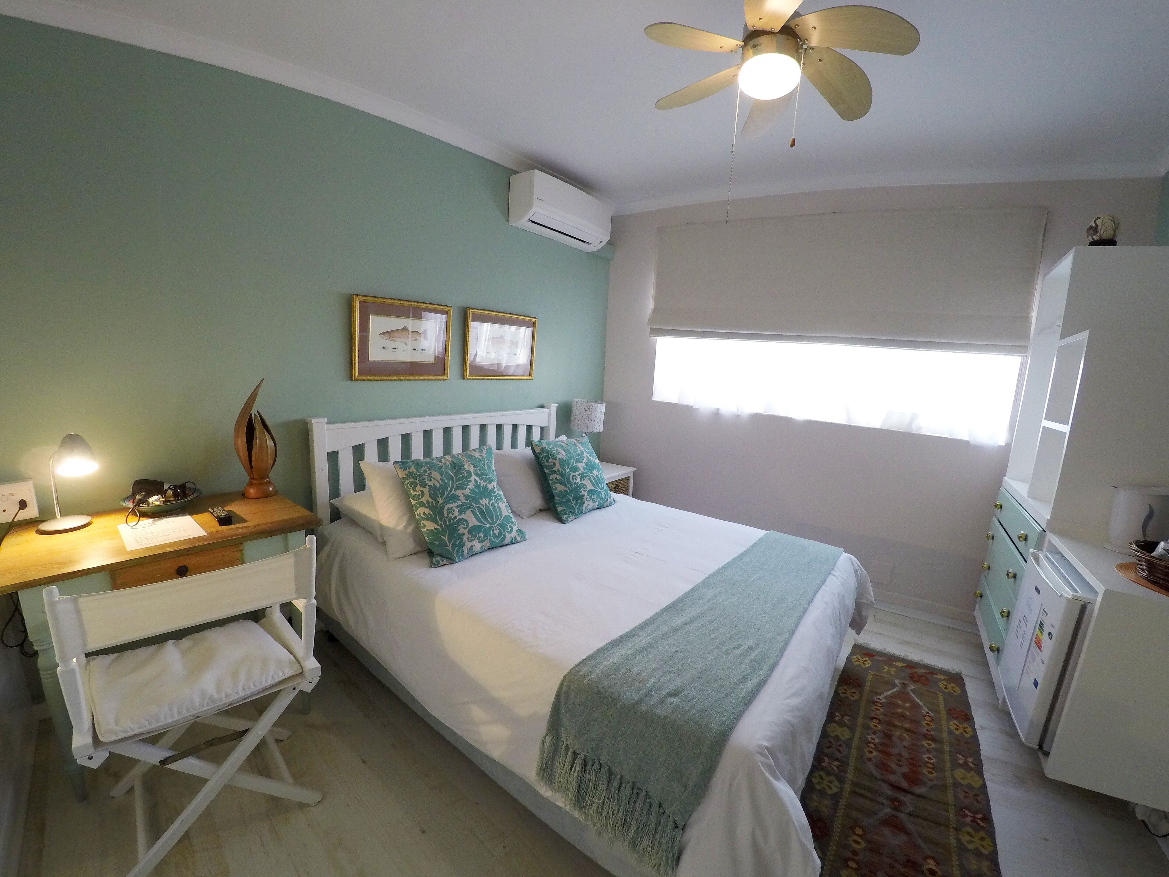 A bedroom with a bed, bedside table, desk, chair, and a ceiling fan.