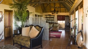 A spacious living room with a high ceiling, a large plant, a sofa, and a dining area with a chandelier.