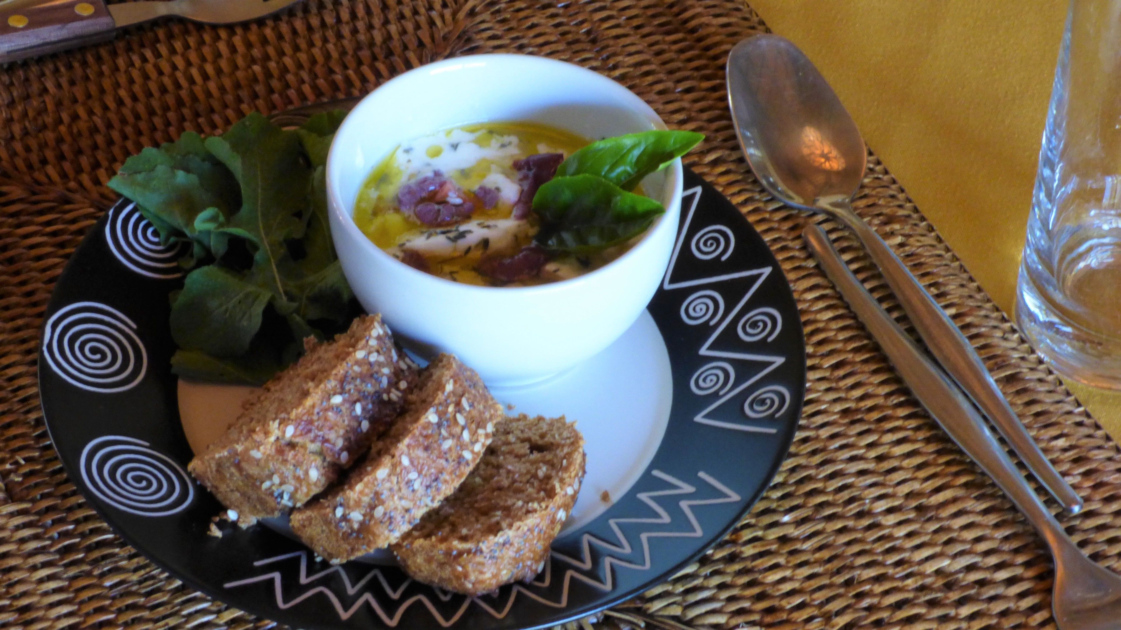 A bowl of soup with a side of bread and greens on a patterned plate.