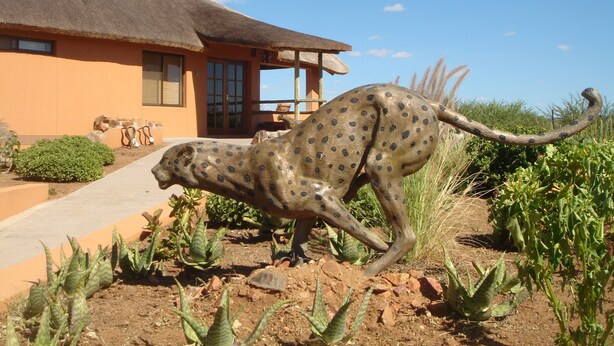 A cheetah statue in a garden with a house in the background.