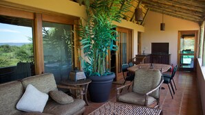 A spacious living area with a large potted plant, comfortable seating, a dining table, and a TV.