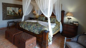 A four-poster canopy bed with floral bedding, a wooden bench, a nightstand with a lamp, and a mirror on the wall.