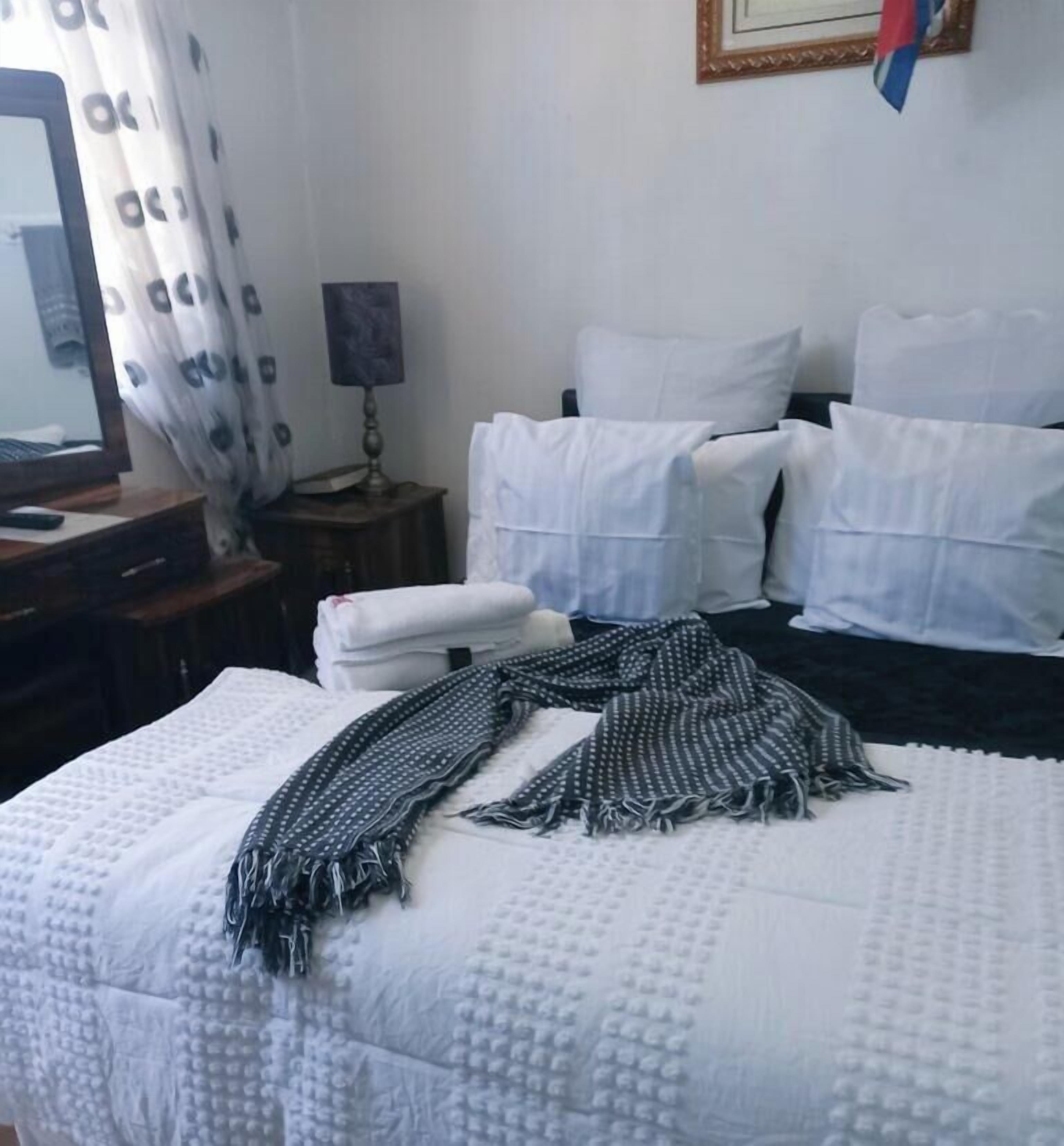 Habitación de hotel con cama, almohadas, una colcha, escritorio, espejo, lámpara y una bandera.