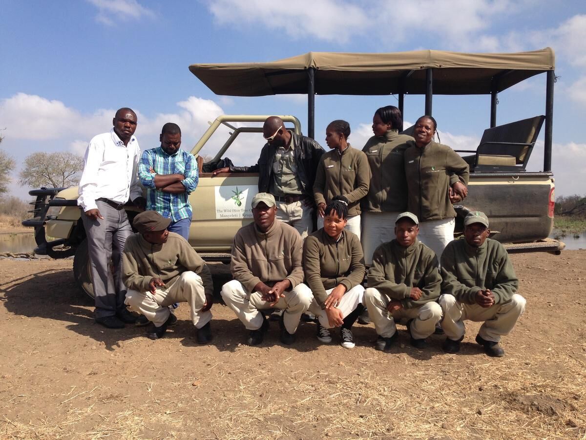 Um grupo de pessoas sentadas e em pé em frente a um veículo de safari.