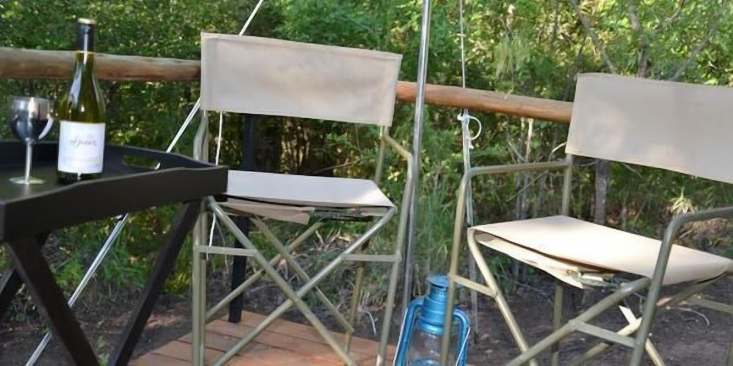 A metal-framed table with a wine bottle and glass, and two folding chairs.
