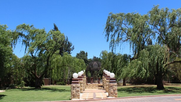 A stone archway with a gazebo in the center, surrounded by lush greenery and trees. - The Willow Tree Guest House (Klerksdorp)