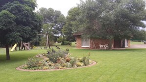 A well-maintained garden with a play area, including a slide and swings, and a small brick building with outdoor seating. - The Willow Tree Guest House (Klerksdorp)