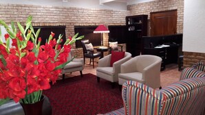 A living room with brick walls, a fireplace, two armchairs, a striped sofa, and a red rug. - The Willow Tree Guest House (Klerksdorp)