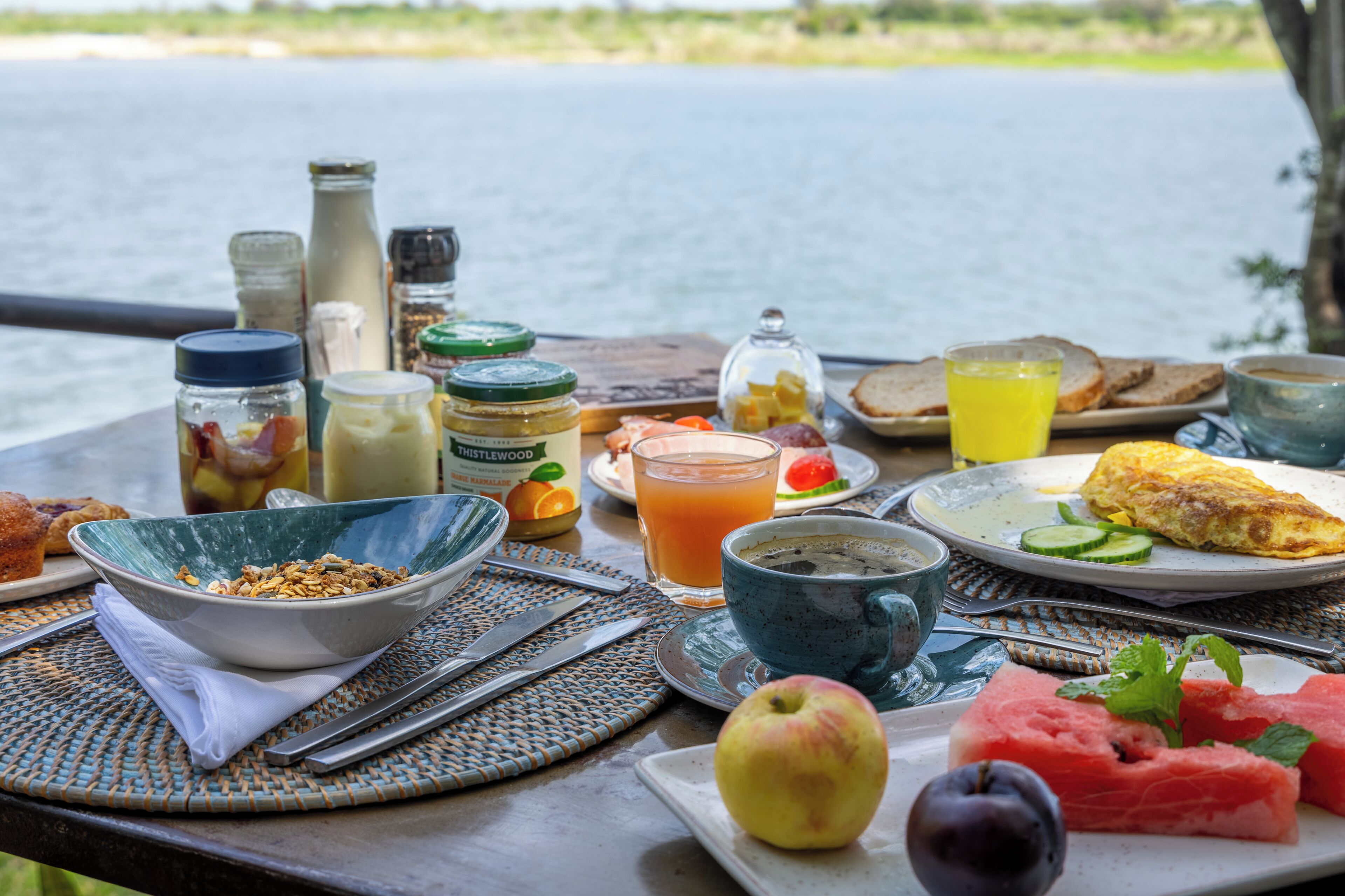 A breakfast table with various food items, a glass of orange juice, and condiments.