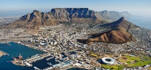 Vista aérea de una ciudad costera con una montaña destacada, un puerto deportivo y un estadio.