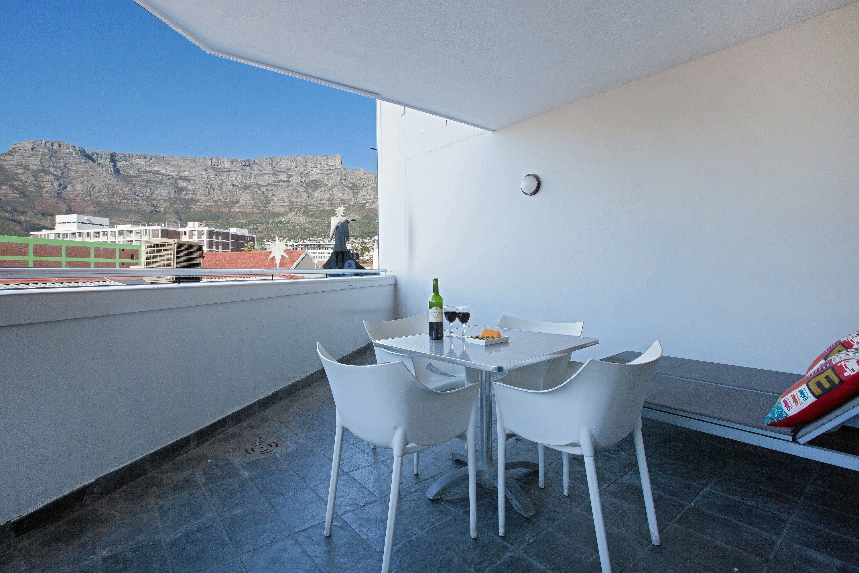 Ein Balkon mit Tisch und Stühlen, einer Weinflasche und Blick auf Gebäude sowie einen Berg.