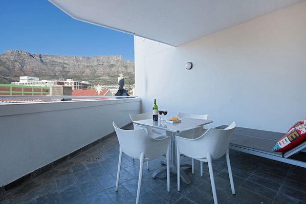 Un balcón con una mesa y sillas, una botella de vino y vistas a edificios y una montaña.