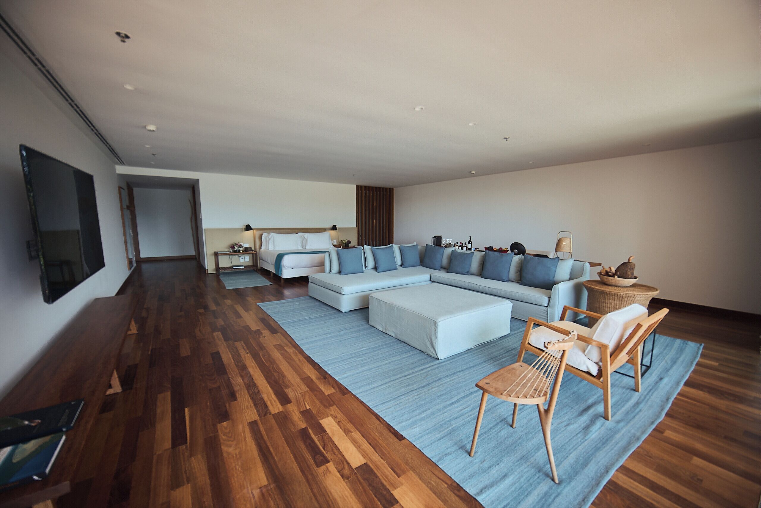 A spacious living area with a large L-shaped sectional sofa, a wooden coffee table, and a wicker chair. A flat-screen TV is mounted on the wall.