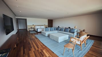 A spacious living area with a large L-shaped sectional sofa, a wooden coffee table, and a wicker chair. A flat-screen TV is mounted on the wall.