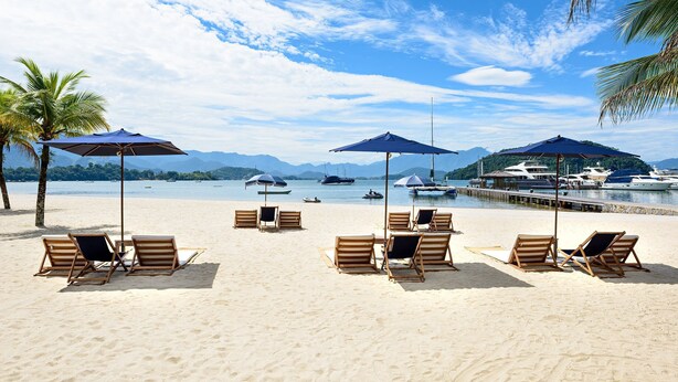 A beach with wooden lounge chairs and umbrellas, a dock with boats, and a clear sky.