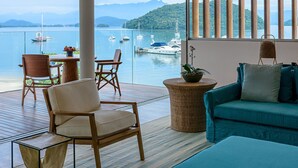 A balcony with a view of the sea, featuring a wooden chair, a blue sofa, and a wicker side table.