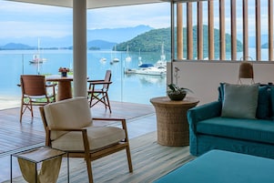 Varanda com vista para o mar, com uma cadeira de madeira, um sofá azul e uma mesa lateral de vime.