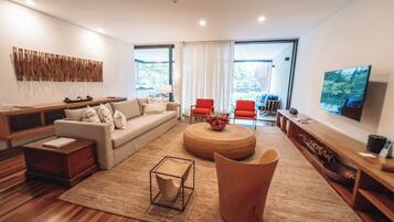 Una sala moderna con sofá, mesa de centro y sillas. Hay un televisor montado en la pared y una ventana que proporciona luz natural.
