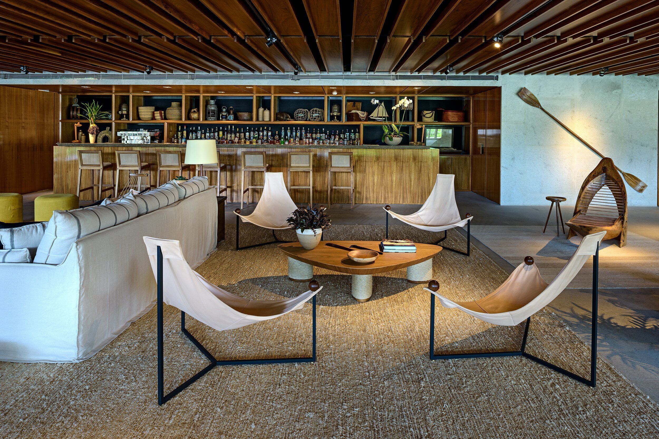 A modern lounge area with a sofa, hammocks, a coffee table, and a bar with shelves of bottles.