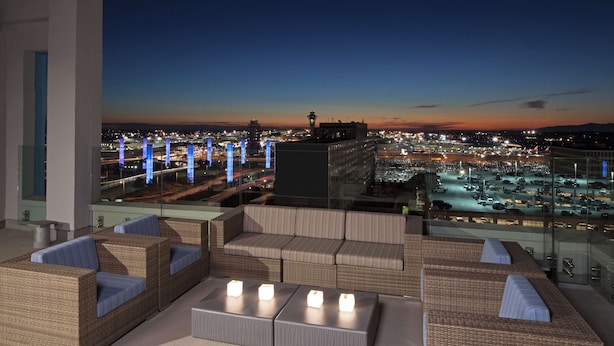 A rooftop lounge with wicker furniture and a view of a cityscape at dusk. - H Hotel Los Angeles, Curio Collection by Hilton (Los Angeles)