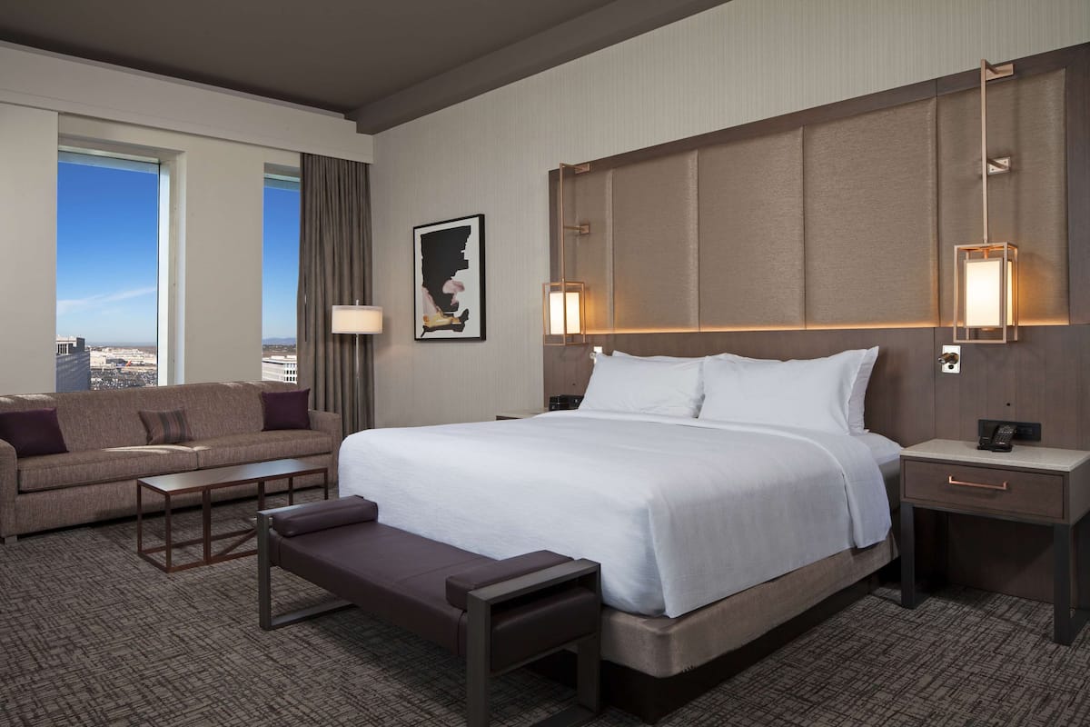 Une chambre d’hôtel avec un grand lit, un canapé, une petite table et une table de chevet avec une lampe.