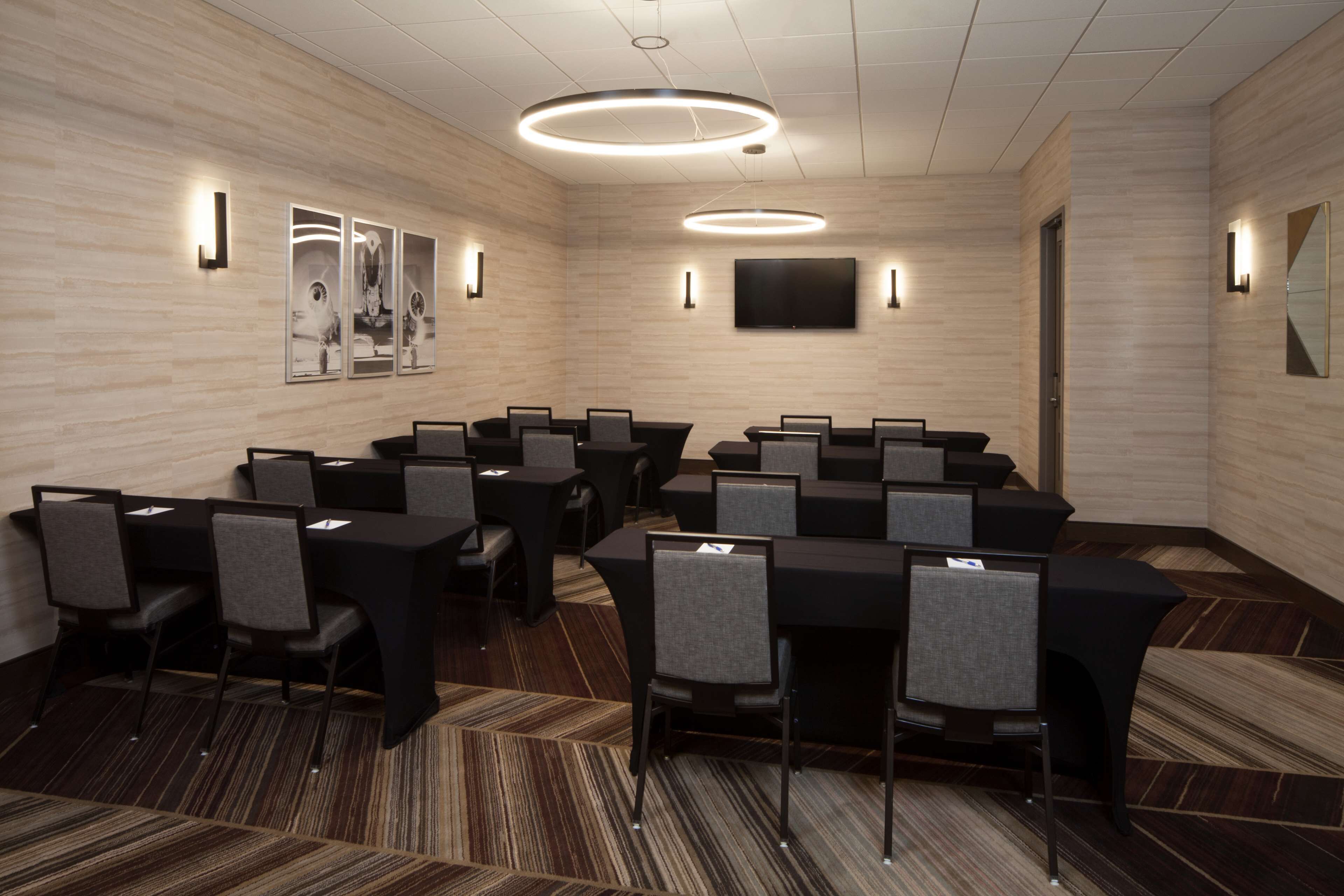 Un salón de conferencias con diseño moderno, con una gran mesa rodeada de sillas, un televisor de pantalla plana montado en la pared y luminarias de luz ambiental.