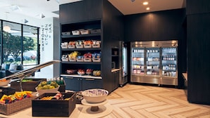 A modern kitchen area with a wooden herringbone floor, a central island with a bowl of fruit, and a refrigerator stocked with beverages. - H Hotel Los Angeles, Curio Collection by Hilton (Los Angeles)