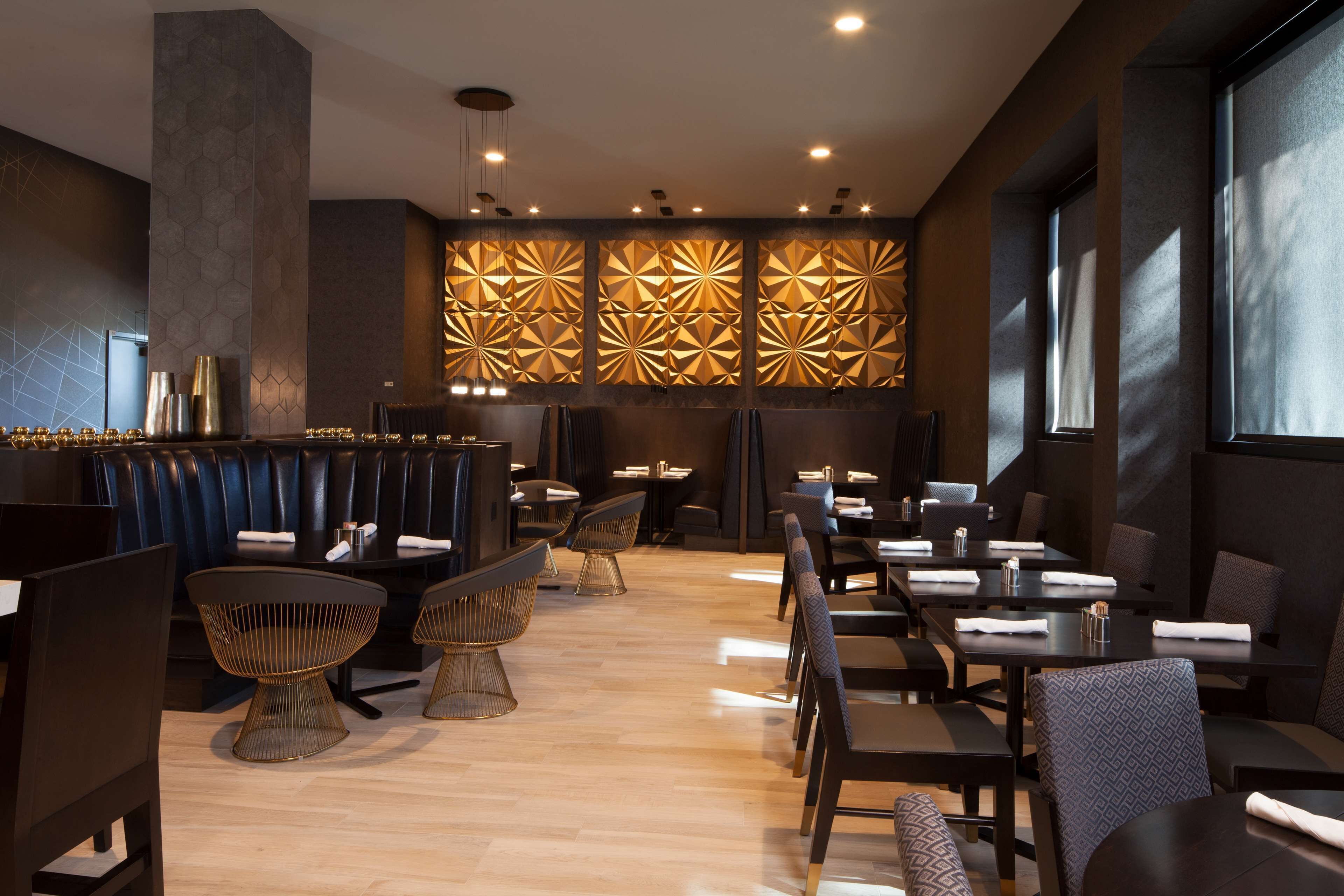 A modern restaurant interior with dark-toned booths, contemporary chairs, and a patterned wall feature.