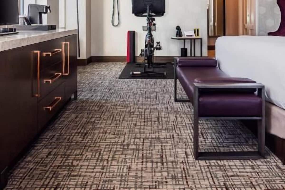 Une chambre d’hôtel avec un lit, un bureau doté d’une machine à café, un téléviseur fixé au mur et une moquette à motifs.