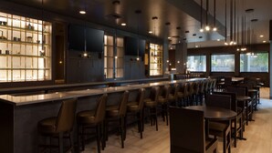 A modern bar area with a long counter, multiple bar stools, and a large window providing natural light. - H Hotel Los Angeles, Curio Collection by Hilton (Los Angeles)