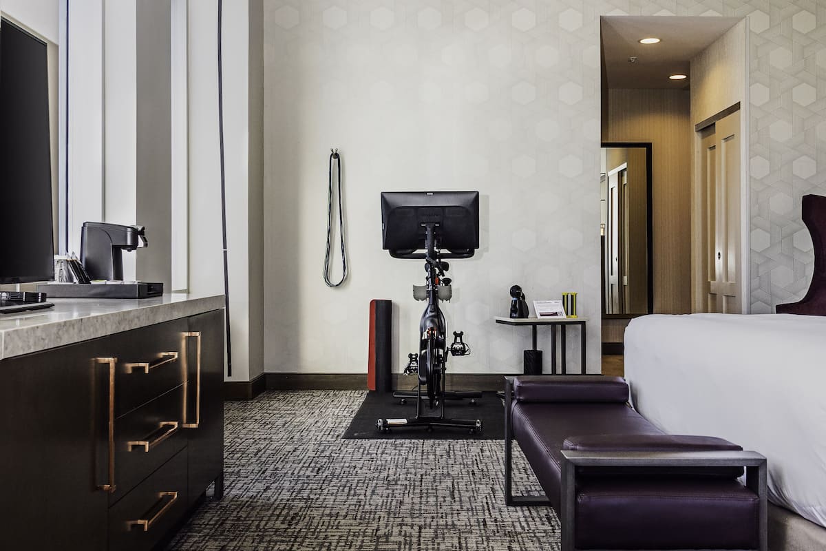 Une chambre d’hôtel équipée d’un lit, d’un bureau avec une machine à café, d’un téléviseur fixé au mur et d’un tapis de course.