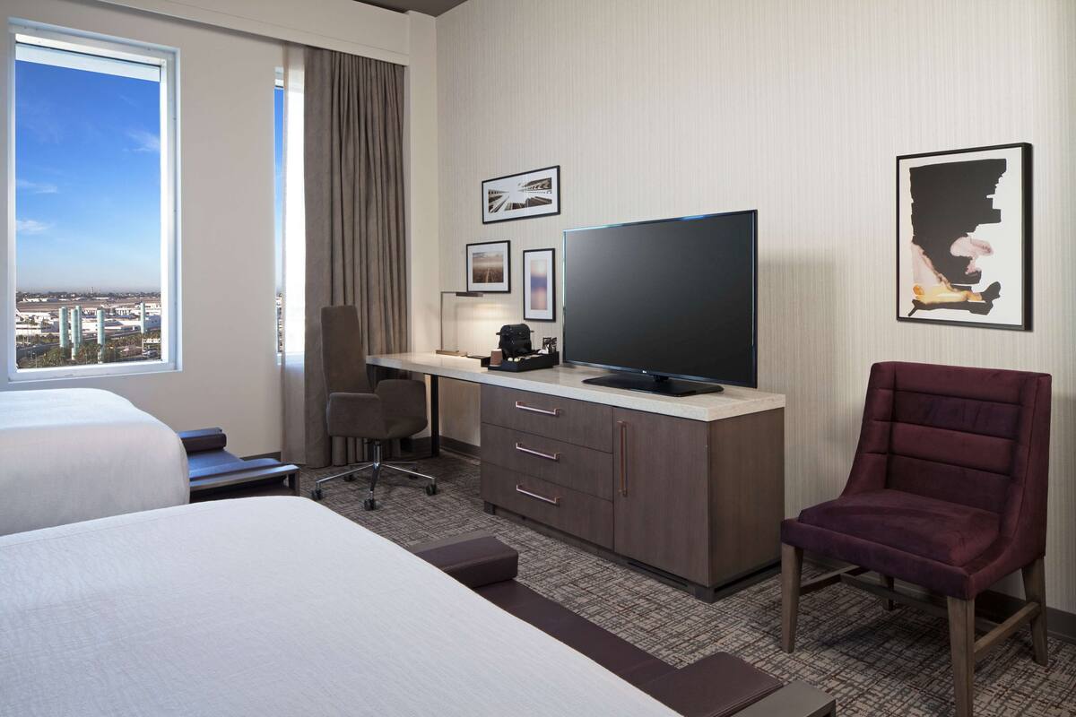 Une chambre d’hôtel équipée d’un lit, d’un bureau, d’une chaise, d’une télévision et offrant une vue sur la ville.
