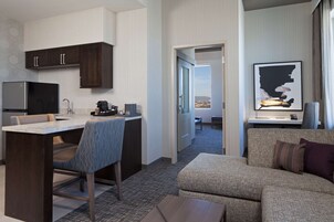 Habitación de hotel con kitchenette, zona de comedor, sofá y ventana grande con vistas.