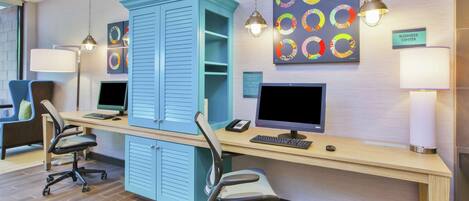 A modern office space with two desks, chairs, a large blue cabinet, and artwork on the wall.