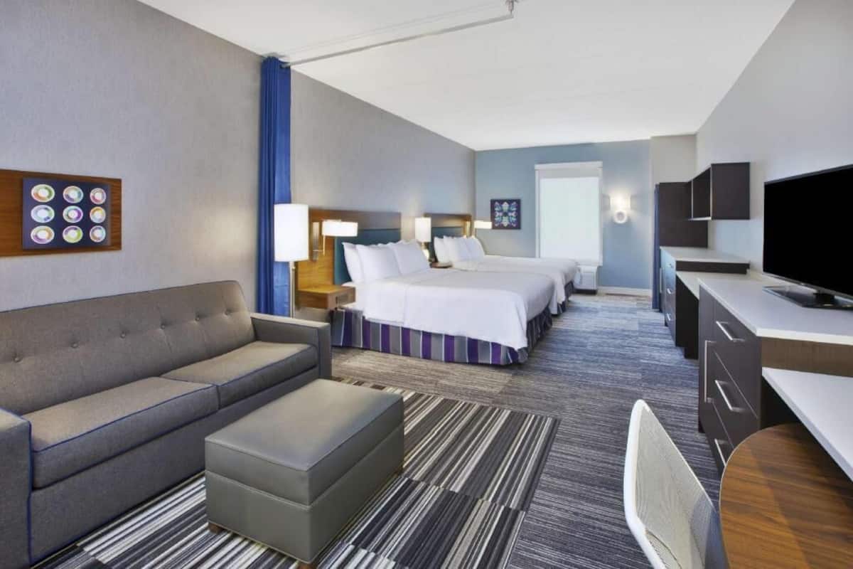 Een hotelkamer met een bank, twee bedden, een bureau, een televisie en een kunstwerk aan de muur.