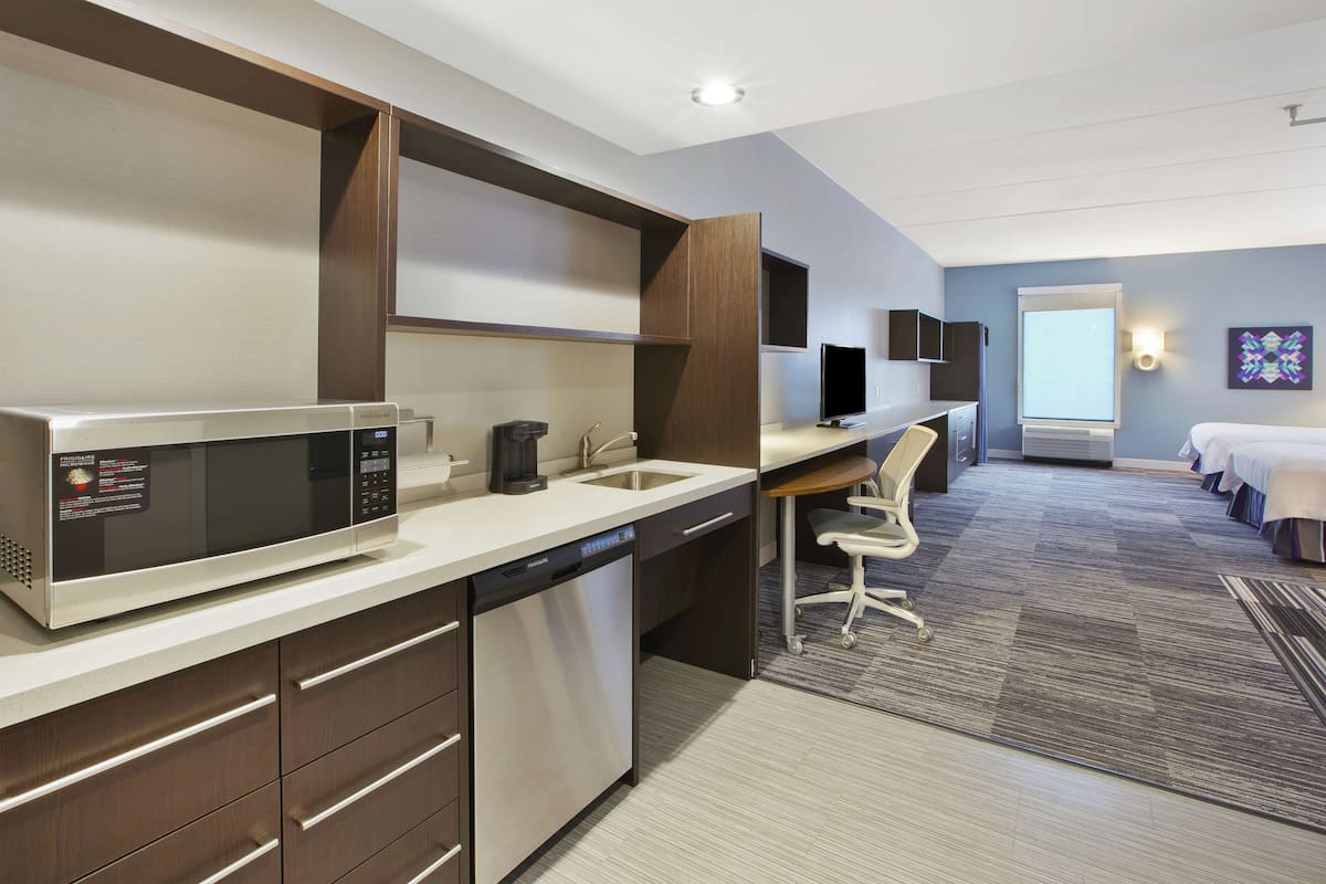 Een moderne hotelkamer met kitchenette, bureau, stoel, bed en uitzicht op de stad.