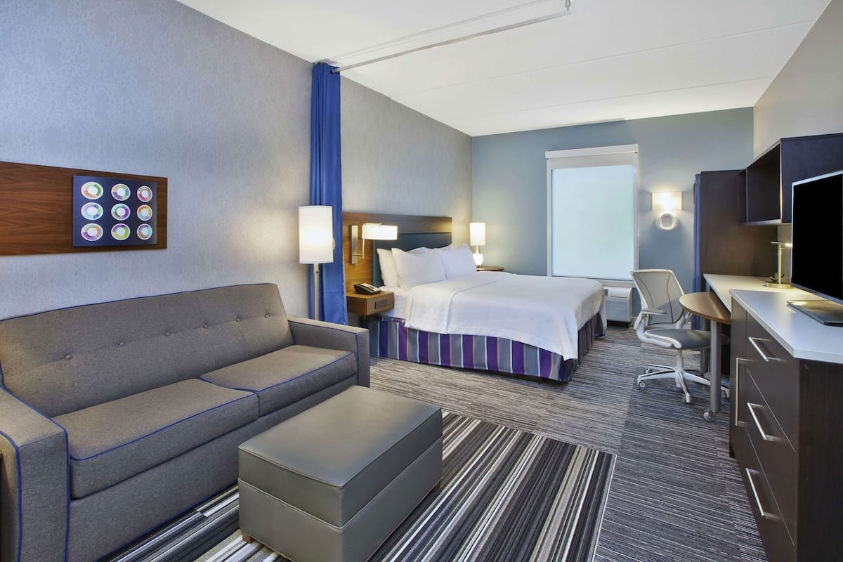 Een hotelkamer met een bed, een bank, een bureau, een televisie en een raam.