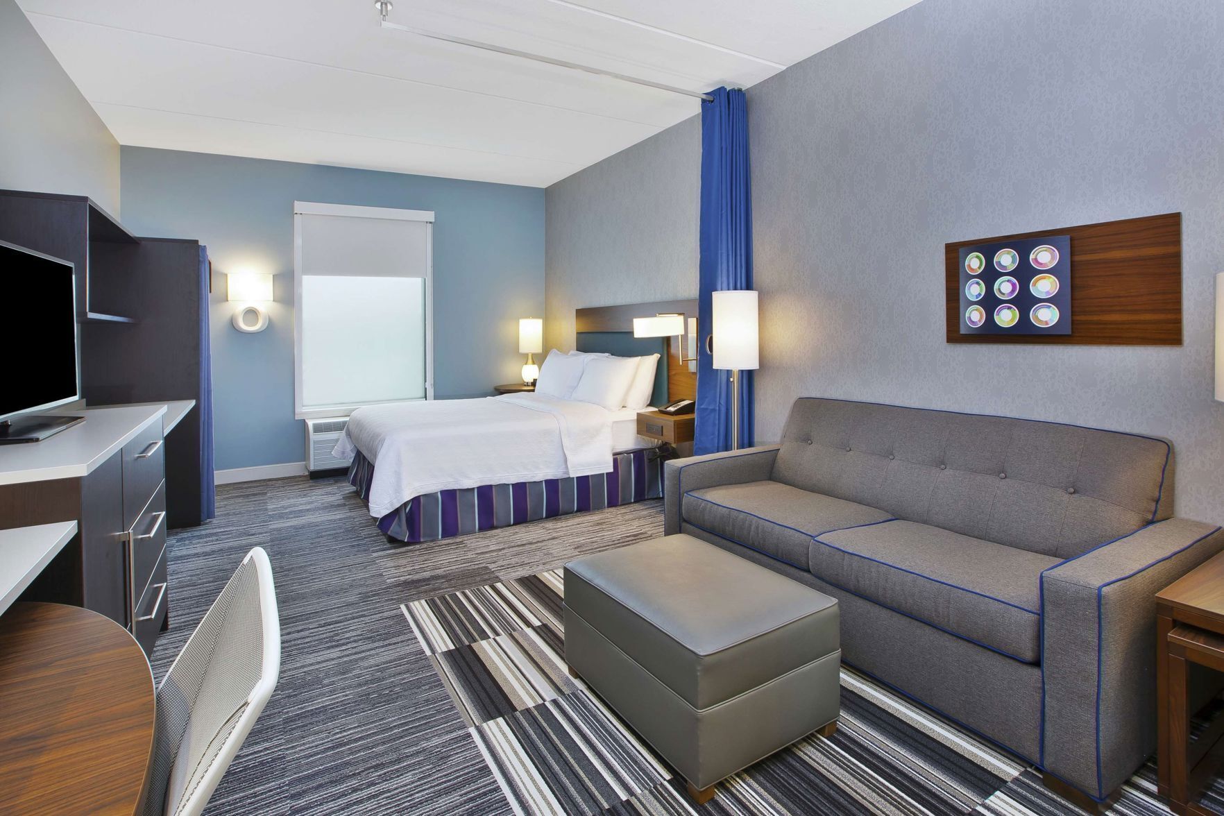 Hotelkamer met een bed, een bank, een bureau met een televisie, een stoel, een lamp en een kunstwerk aan de muur.