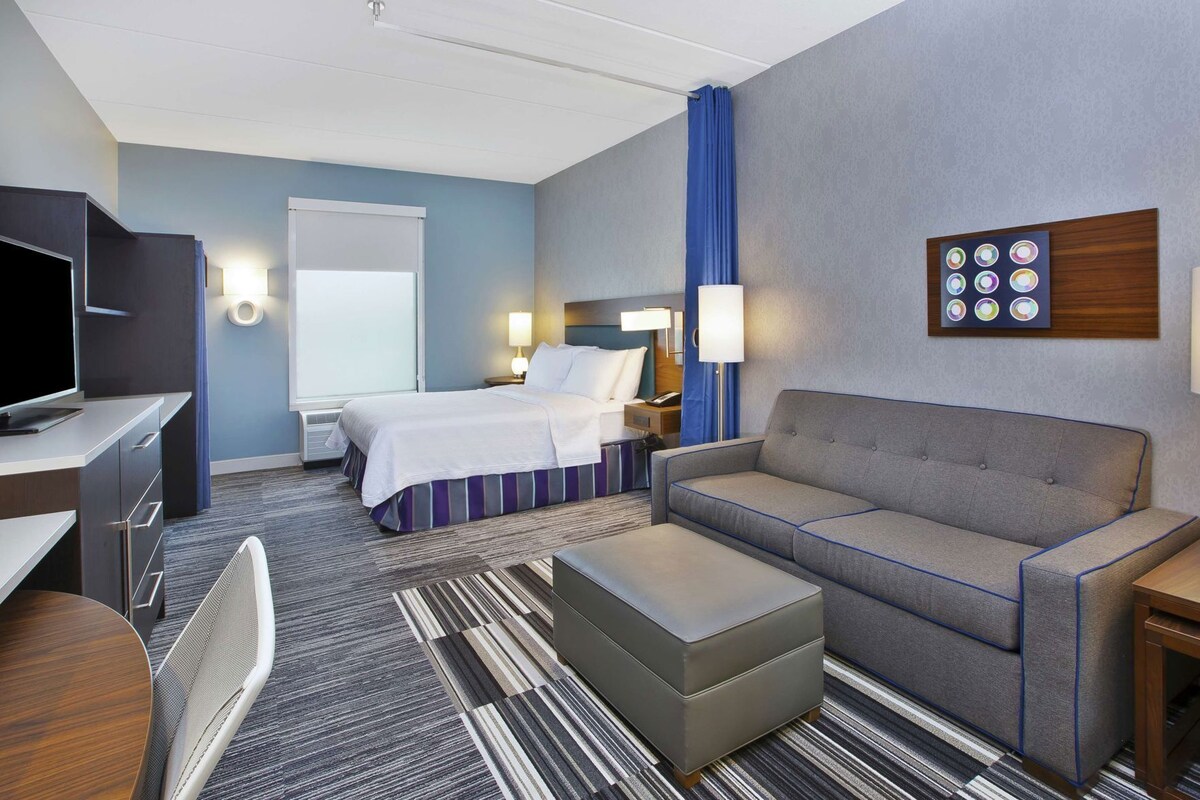 Hotelkamer met een bed, een bank, een bureau met een televisie, een stoel, een lamp en een kunstwerk aan de muur.