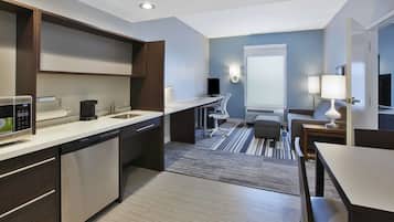 Una cocina moderna con lavavajillas, microondas y cafetera. Hay un comedor con mesa y sillas, y un ventanal que proporciona luz natural.
