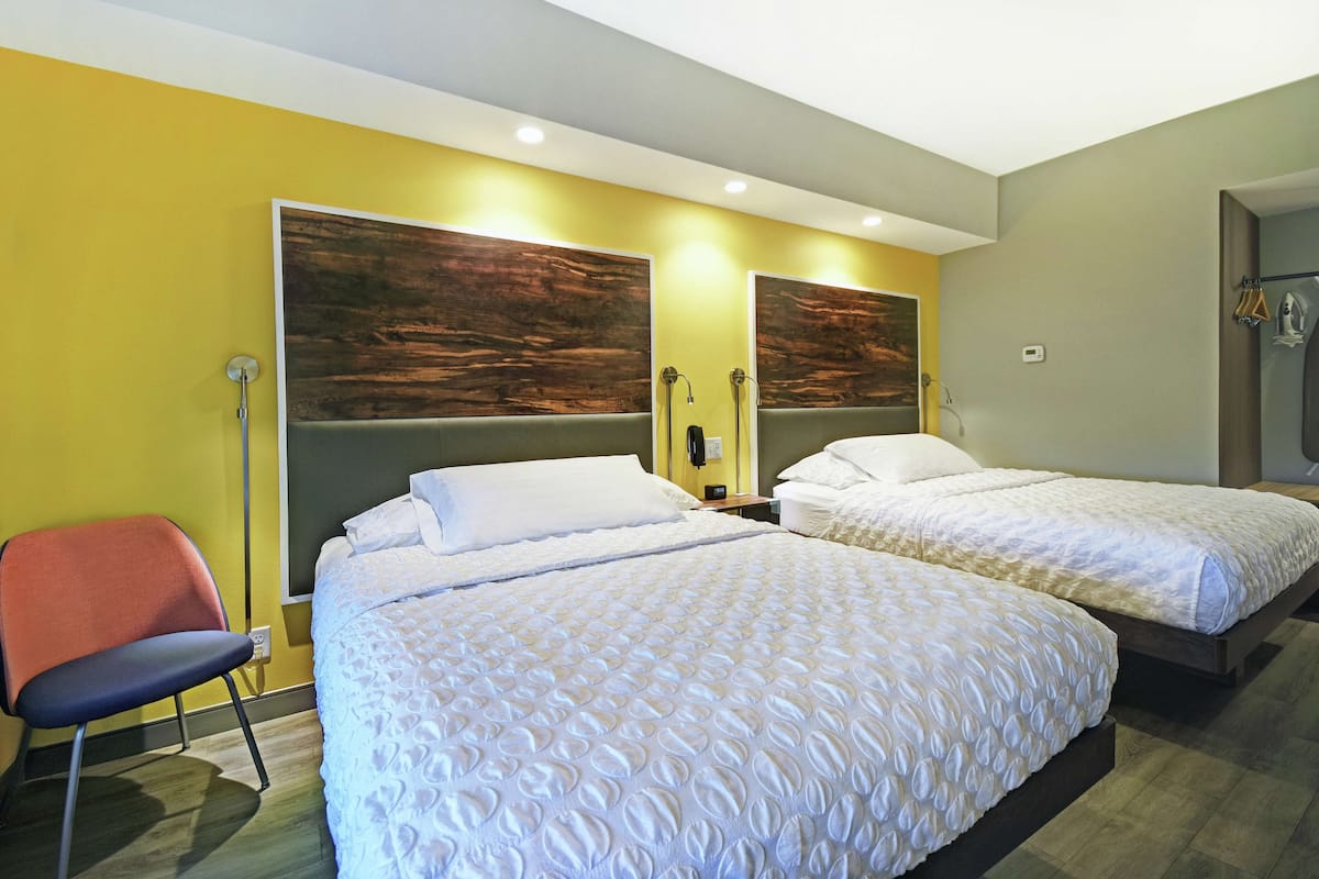 Une chambre d’hôtel avec deux lits, une chaise et une tête de lit en bois.